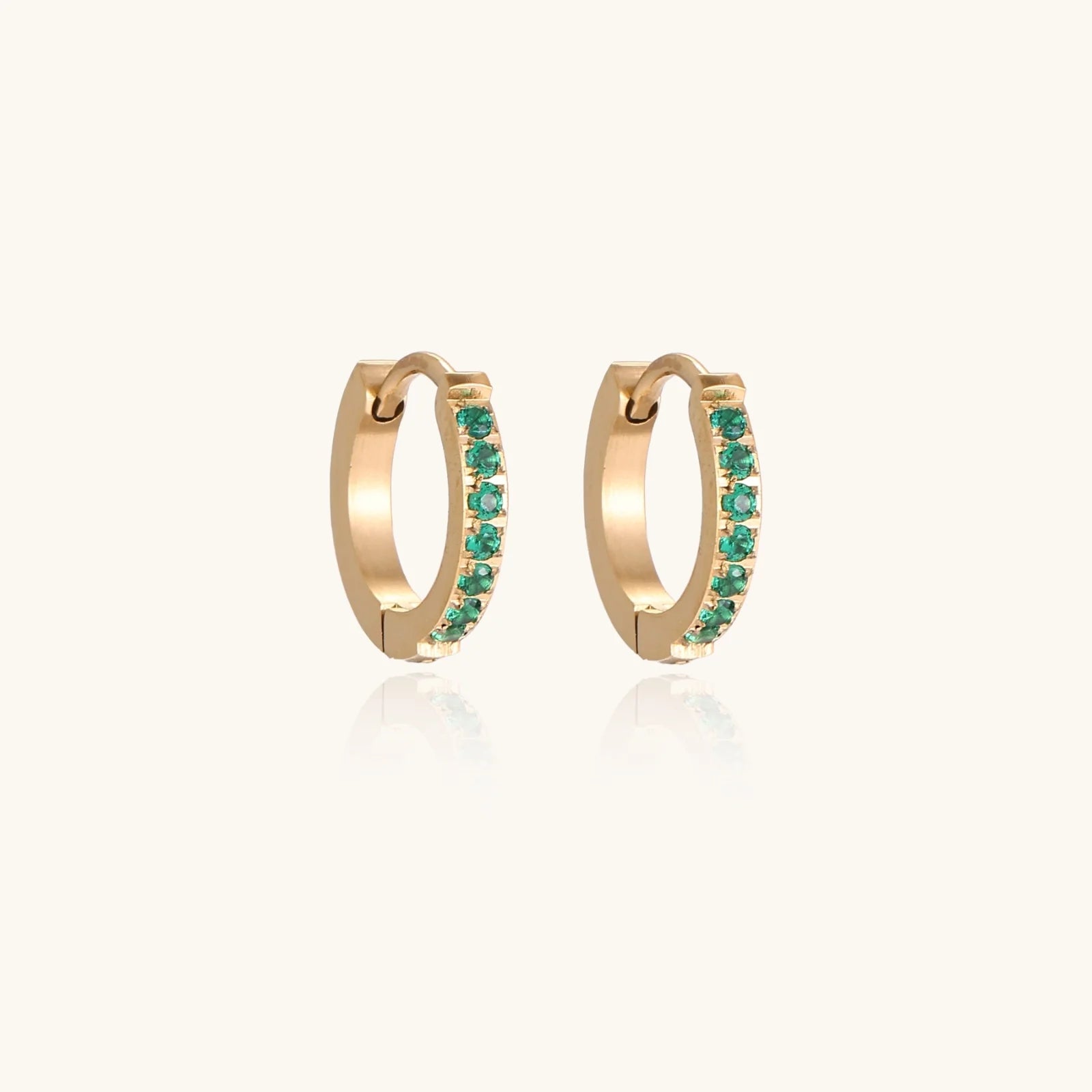 Pair of small gold huggie hoop earrings with bright green cubic zirconia stones on cream background