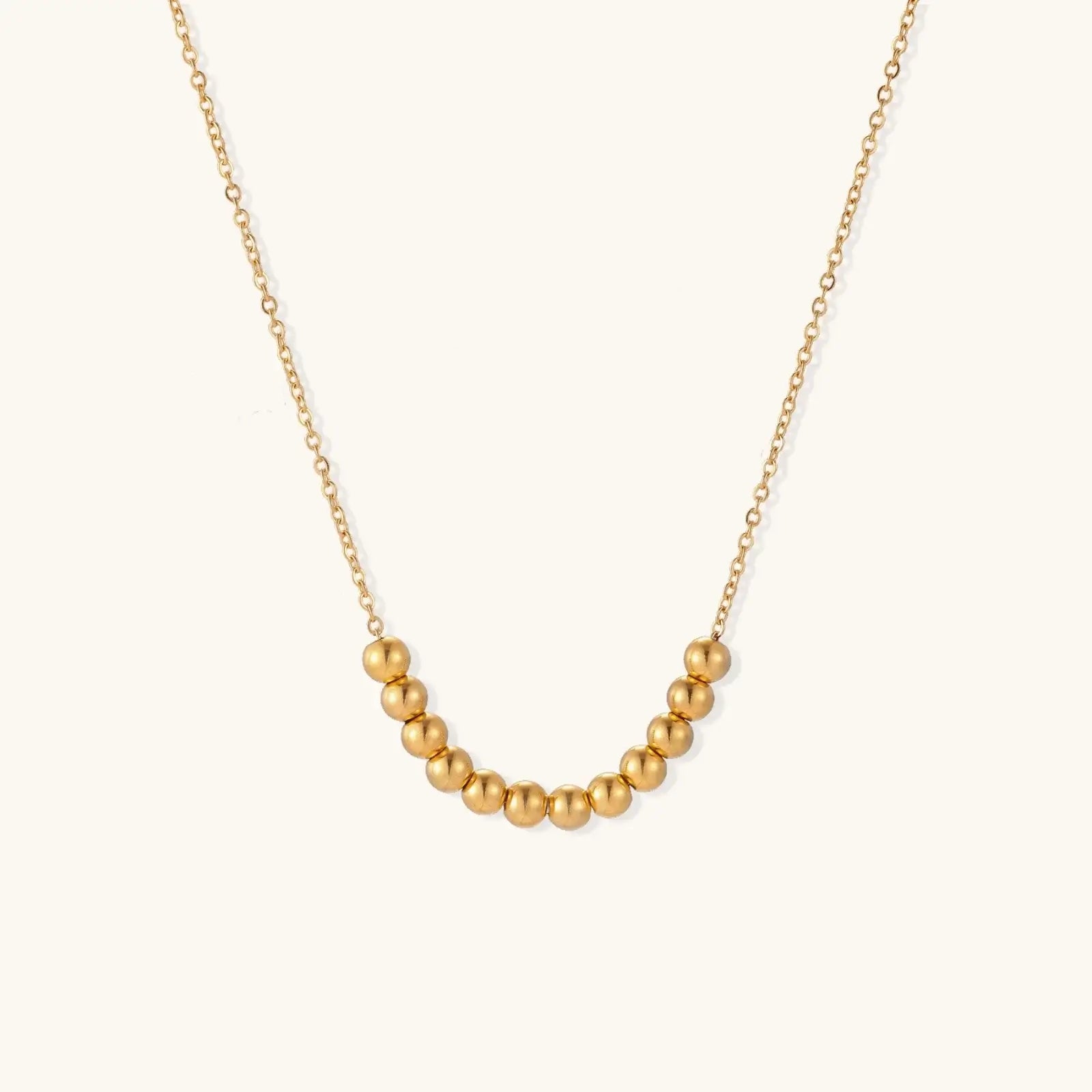 Delicate gold-plated necklace with graduated spherical beads forming gentle smile curve on beige background
