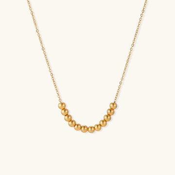 Delicate gold-plated necklace with graduated spherical beads forming gentle smile curve on beige background
