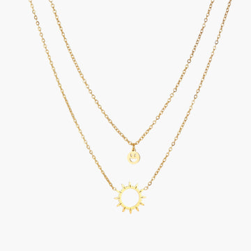 Gold layered necklace set with sunburst and smiley face pendants on delicate chains against white background.